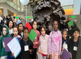 Students spread out with clipboards i front of a rock